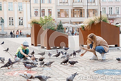 Young mother with baby with pigeons. Beautiful woman with her son near the birds. Pigeons in the city. Stock Photo