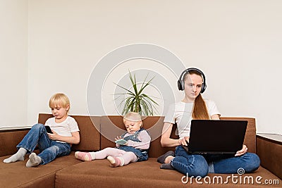 Young mother with computer in hand and kids with phones sitting on couch. Overuse of devices Stock Photo