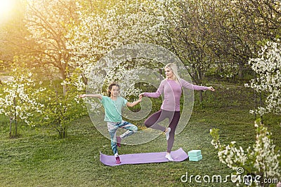 a young mother and daughter perform yoga exercises in the park on a gym mat. healthy lifestyle. Stock Photo