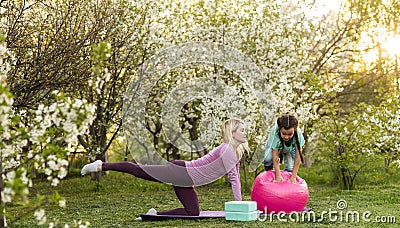 a young mother and daughter perform yoga exercises in the park on a gym mat. healthy lifestyle. Stock Photo