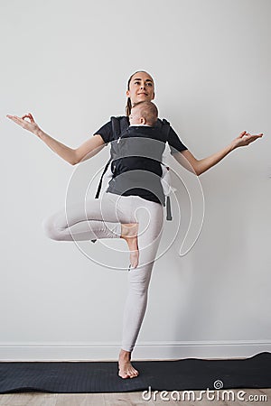 Young mother doing yoga with baby in ergo backpack Stock Photo