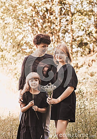 Young mother embraces two daughters on nature in summer. Girls hug together, laugh, have fun. Traveling with children, maternal Stock Photo