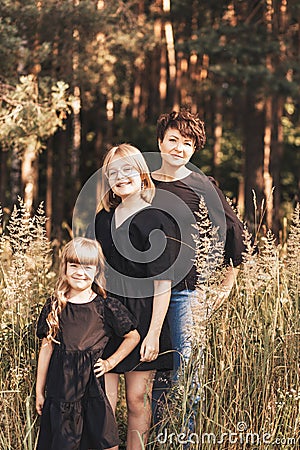 Young mother embraces two daughters on nature in summer. Girls hug together, laugh, have fun. Traveling with children, maternal Stock Photo