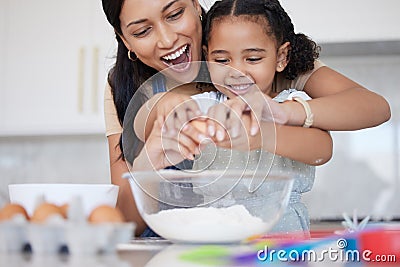 Young mother enjoying baking, bonding with her little daughter in the kitchen at home. Little latino girl smiling while Stock Photo