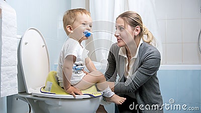 Young mother explaining to her toddler son how to use toilet Stock Photo