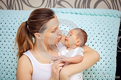 Young mother gently hugs her newborn baby. Mothers Day. Woman kisses baby Stock Photo