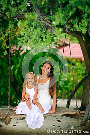 Young mother and her daughter swinging at tropic Stock Photo