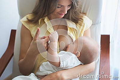 Young mother holding her baby boy, brestfeeding him, sitting in Stock Photo