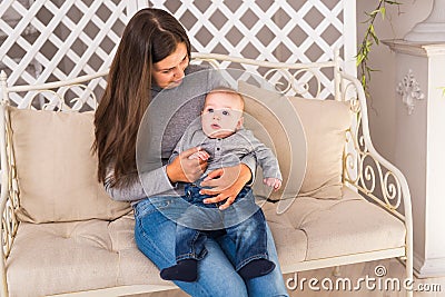 Young mother holding her newborn child. Woman and baby boy relax in a white bedroom. Nursery interior. Family at home Stock Photo