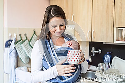 Young mother in kitchen with her son in sling Stock Photo