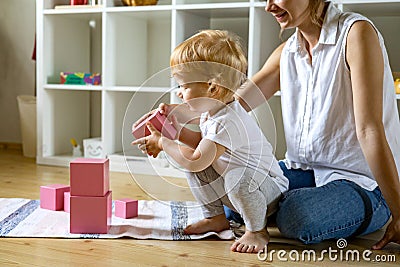 Young mother and little baby assembling pink cube Maria Montessori ecological materials Stock Photo