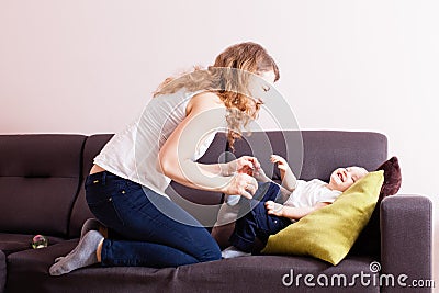 Young mother loughing tickling her adorable toddler son on their couch. Stock Photo