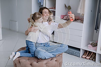 Young mother sits in a modern dressing room with a phone taking selfies with her twin daughters Stock Photo