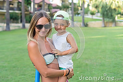 Young mother and smiling baby boy son in green baseball cap playing in the sea in the day time. Positive human emotions, feelings, Stock Photo