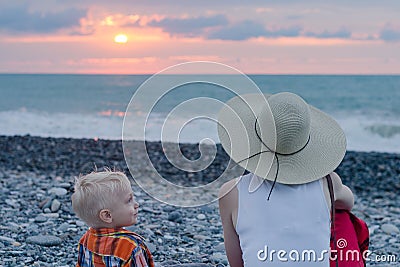 Young mother and son sitting on beach against sea and sunset. Single mother concept Stock Photo