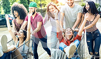 Young multiracial people having fun together with shopping cart - Millenial friends sharing time with trolleys at commercial mall Stock Photo