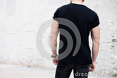 Young muscular bearded man wearing black tshirt and jeans posing in center of modern city. Empty concrete wall on the Stock Photo