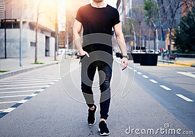 Young muscular man wearing black tshirt and jeans walking on the streets of the modern city. Blurred background Stock Photo