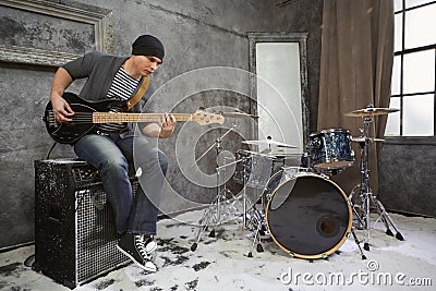 Young musician plays bass electric guitar sitting on amplifier Stock Photo