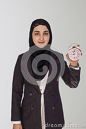 Young Muslim businesswoman in hijab holding pink vintage alarm clock. Middle-eastern businesswoman in abaya holds alarm clock Stock Photo