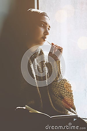 Young Muslim woman sits on the window sill. Middle-eastern writer woman sitting thoughtfully near the window and writing her story Stock Photo