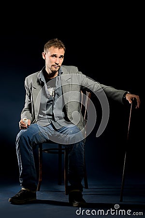 Young negligent man with cane sitting on chair Stock Photo