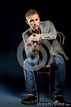 Young negligent man with cane sitting on chair Stock Photo