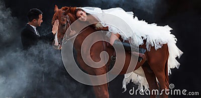 Young newlywed couple, beautiful beauty bride in fashion white bridal wedding costume riding on strong muscular horse standing by Stock Photo