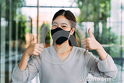 Young optimistic Asian female student giving thumbs up gesture. She`s wearing a protective mask PPE to avoid air Stock Photo