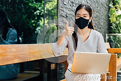 Young optimistic Asian female student giving thumbs up gesture. She`s wearing a protective mask PPE to avoid air Stock Photo