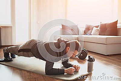 Young ordinary man go in for sport at home. Full size pictrue of freshman in workout and beginner guy stand in plank Stock Photo