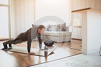 Young ordinary man go in for sport at home. Full size picture of regular ordinary guy stand in plank position alone in Stock Photo
