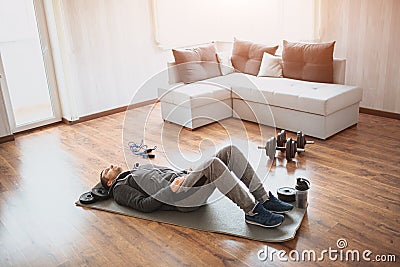 Young ordinary man go in for sport at home. Regular beginner lying on mat on floor and has rest. Real picture of guy Stock Photo