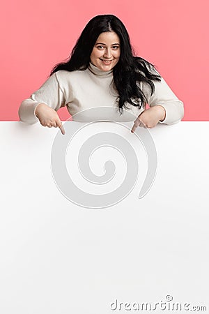 Young overweight woman pointing at white blank advertisement board Stock Photo