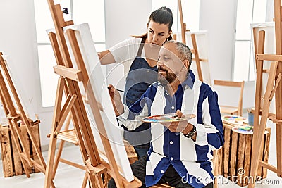 Young painting teacher woman teaching art to senior man painting on canvas at art studio Stock Photo