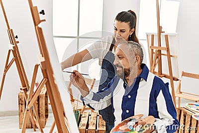 Young painting teacher woman teaching art to senior man painting on canvas at art studio Stock Photo