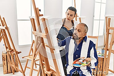 Young painting teacher woman teaching art to senior man painting on canvas at art studio Stock Photo