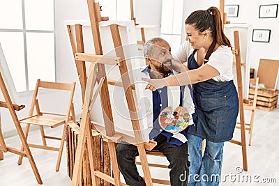 Young painting teacher woman teaching art to senior man painting on canvas at art studio Stock Photo