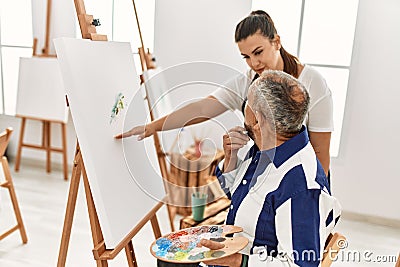 Young painting teacher woman teaching art to senior man painting on canvas at art studio Stock Photo