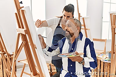 Young painting teacher woman teaching art to senior man painting on canvas at art studio Stock Photo