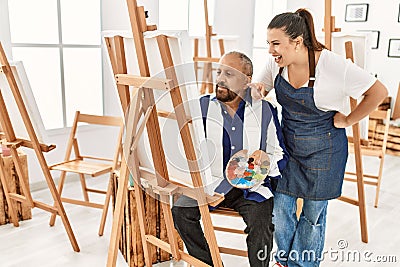 Young painting teacher woman teaching art to senior man painting on canvas at art studio Stock Photo