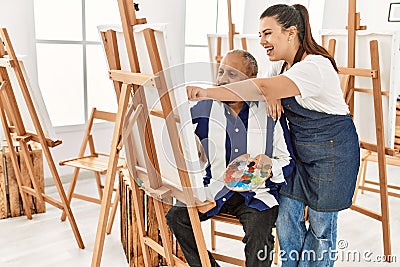 Young painting teacher woman teaching art to senior man painting on canvas at art studio Stock Photo