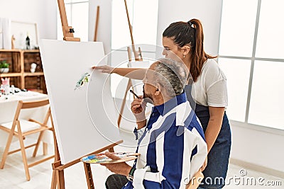 Young painting teacher woman teaching art to senior man painting on canvas at art studio Stock Photo