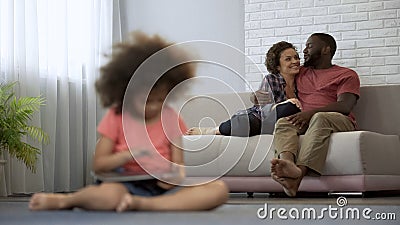 Young parents enjoying joint pastime watching their daughter playing on tablet Stock Photo