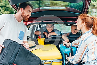 young parents packing luggage in trunk of car with kids Stock Photo