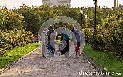 A young parents with strollers walking in the park back side view. Four people in the garden. Editorial Stock Photo