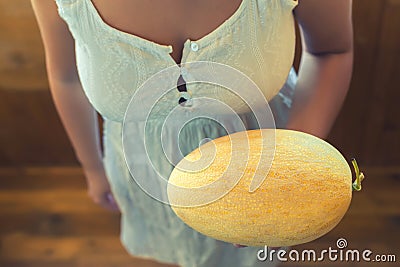 Young peasant girl with big melons in a rustic white dress on a wooden terrace Stock Photo