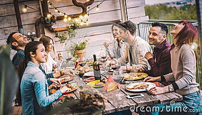 Young people dining and having fun drinking red wine together on balcony rooftop dinner party - Happy friends eating bbq food at Stock Photo