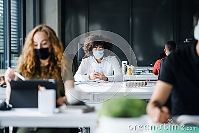 Young people with face masks back at work or school in office after lockdown. Stock Photo