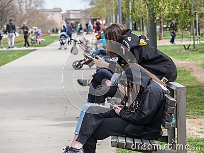 Young people, generation Z teenager girls, sitting on a bench watching their smartphones and looking at its content in the street Editorial Stock Photo